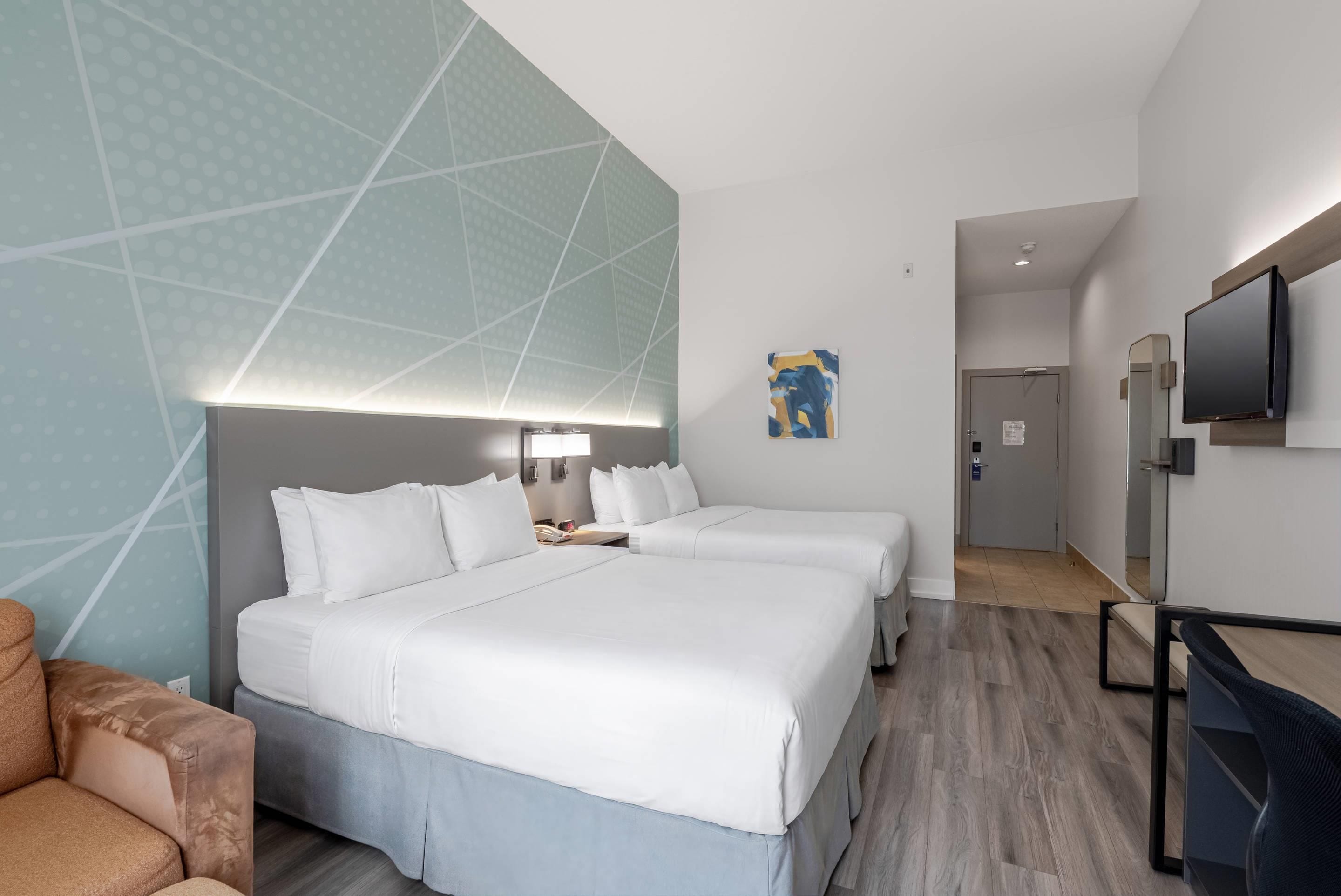 Une chambre d’hôtel avec un grand lit, un bureau, une chaise, une télévision et une porte donnant sur une autre pièce.