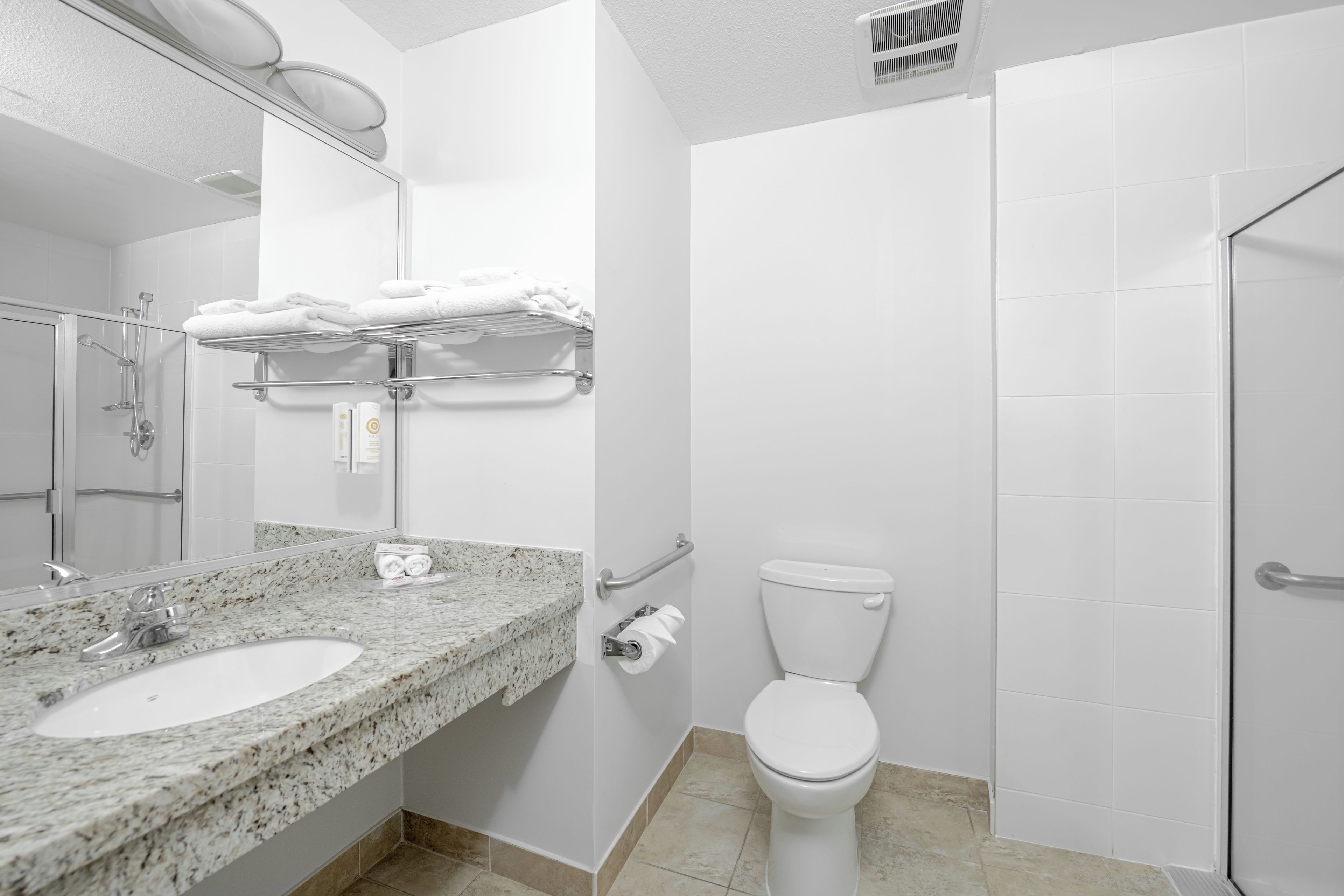 A bathroom with a granite countertop, a white toilet, and a shower area.