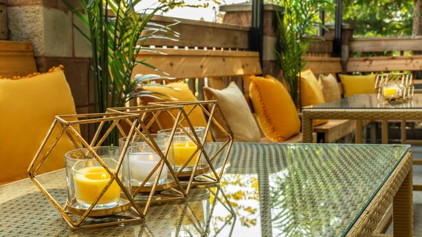 A cozy outdoor seating area with wicker furniture and cushions, a glass-top table, and candles.