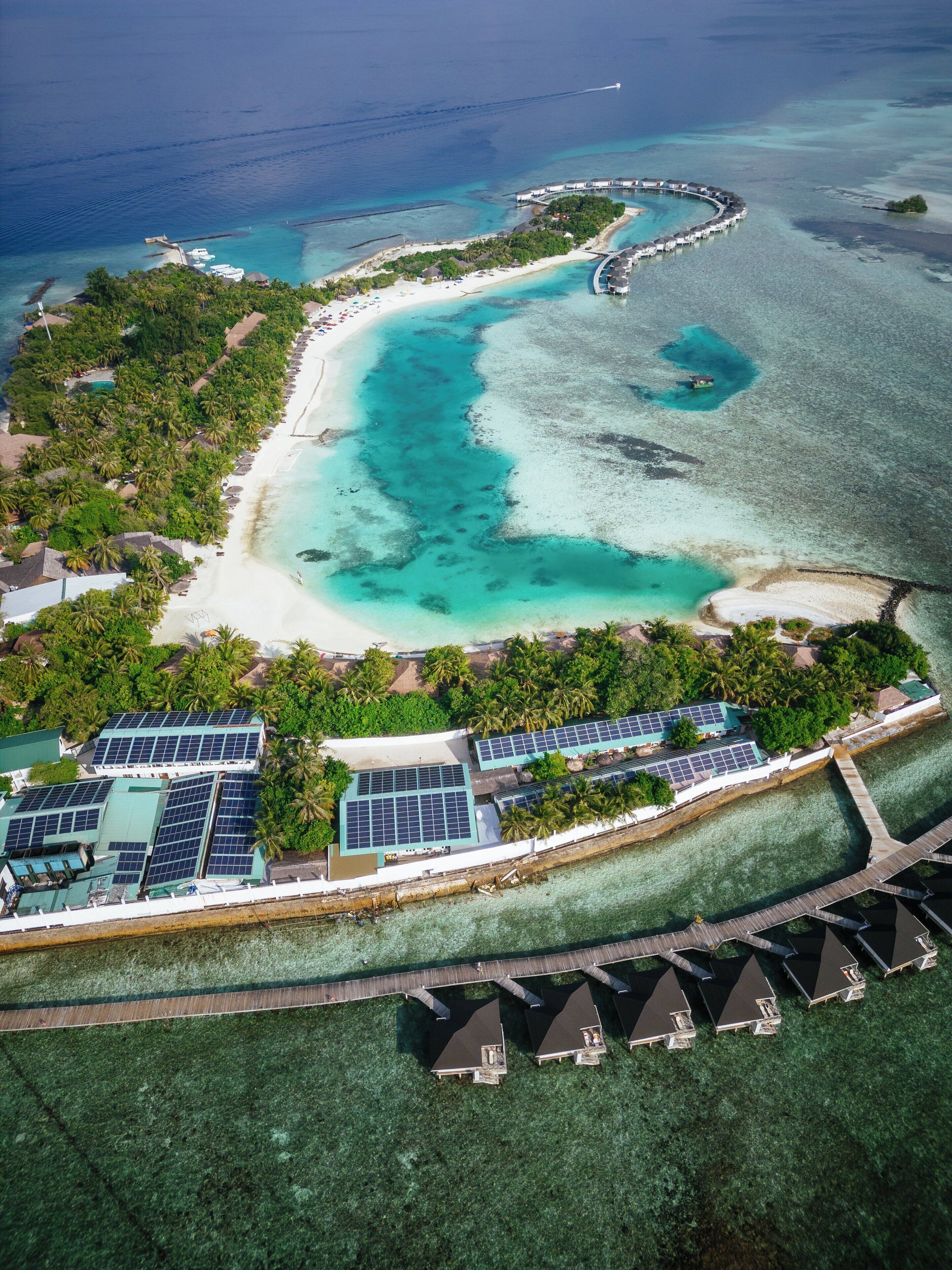 An aerial view of a resort with a beach, clear turquoise waters, and solar panels on buildings.