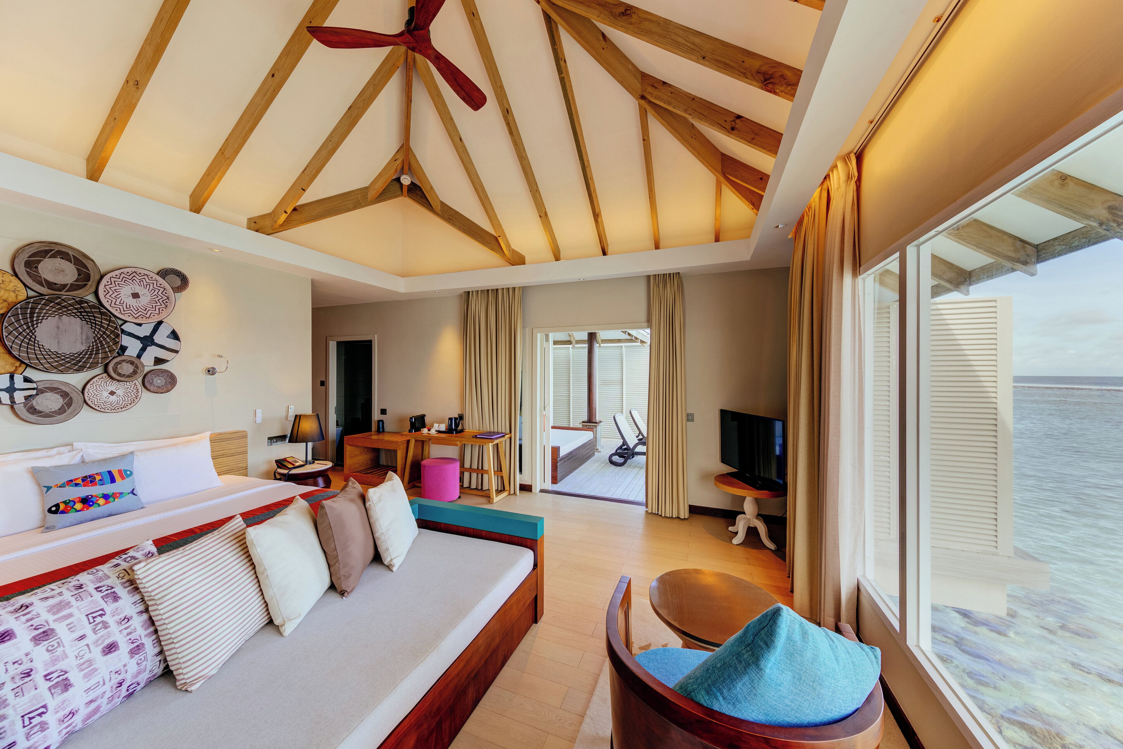 A spacious room with a large bed, a wooden ceiling, a seating area, and a view of the sea.