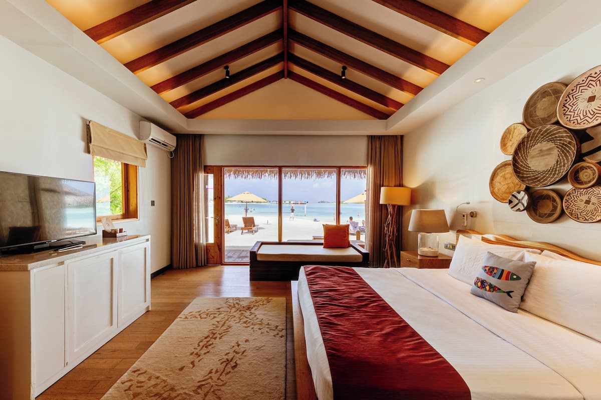 Une chambre d’hôtel avec un lit, une télévision, un bureau et une vue sur la plage.