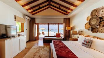 A hotel room with a bed, a TV, a desk, and a view of the beach.