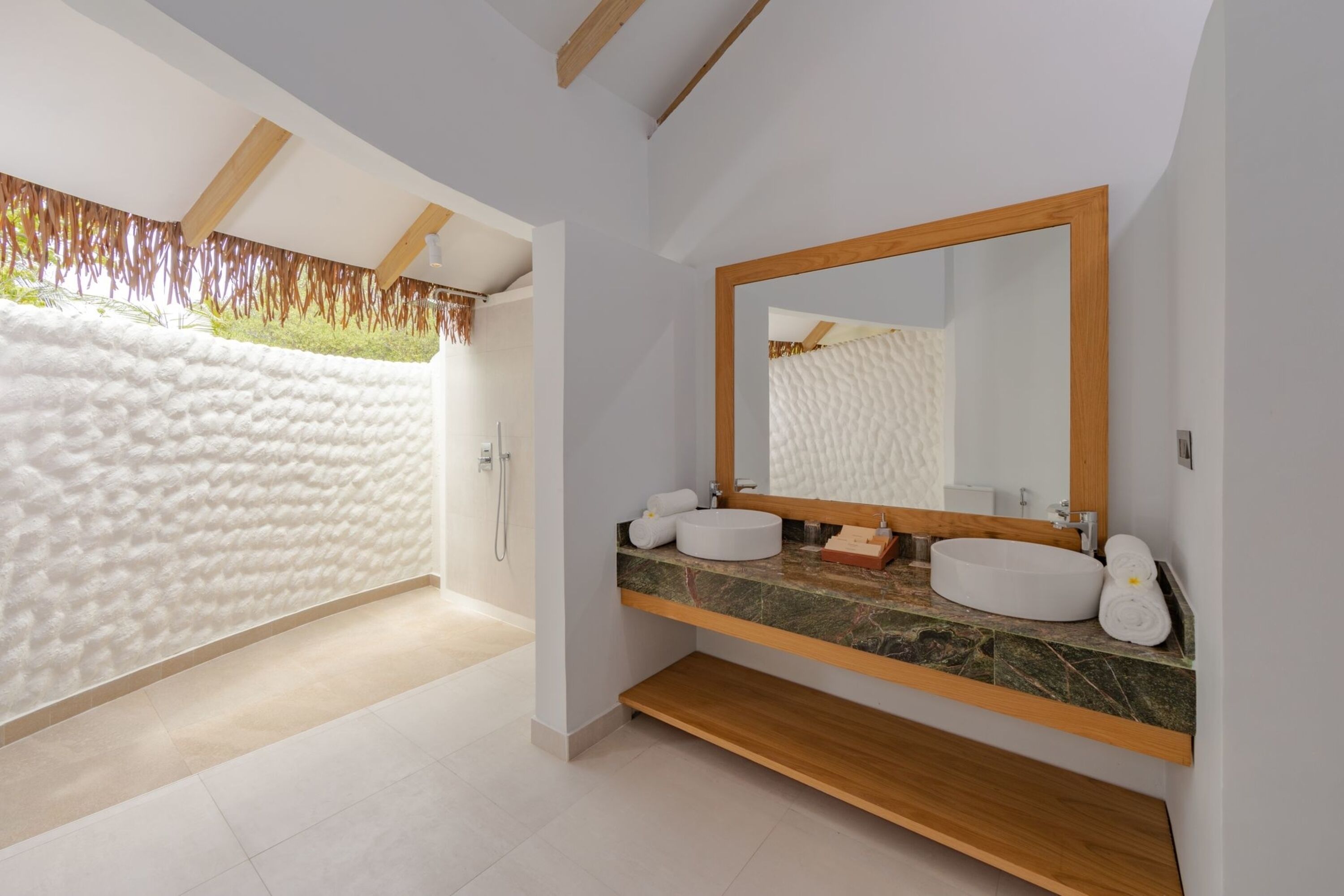 A modern bathroom with a large mirror, two sinks, and a shower area.
