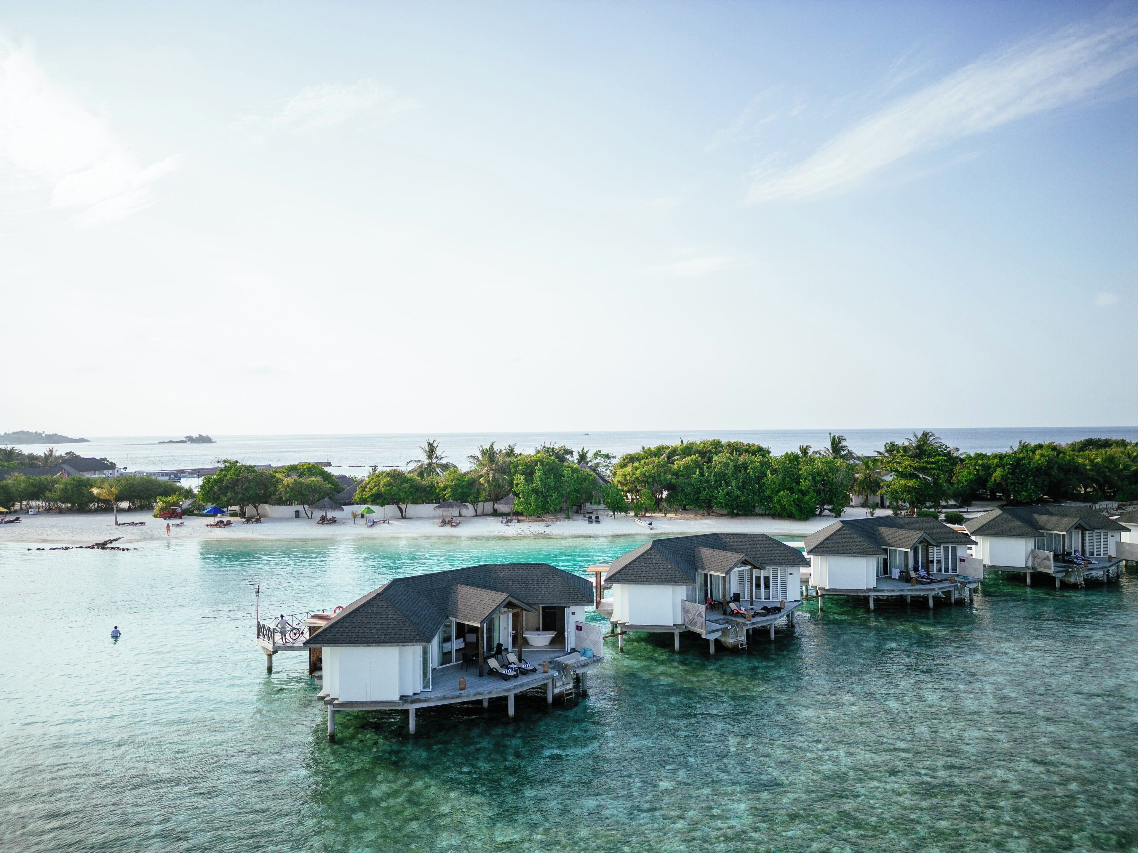 Bungalow sull'acqua con acque turchesi cristalline, una spiaggia sabbiosa e una vegetazione rigogliosa sullo sfondo.
