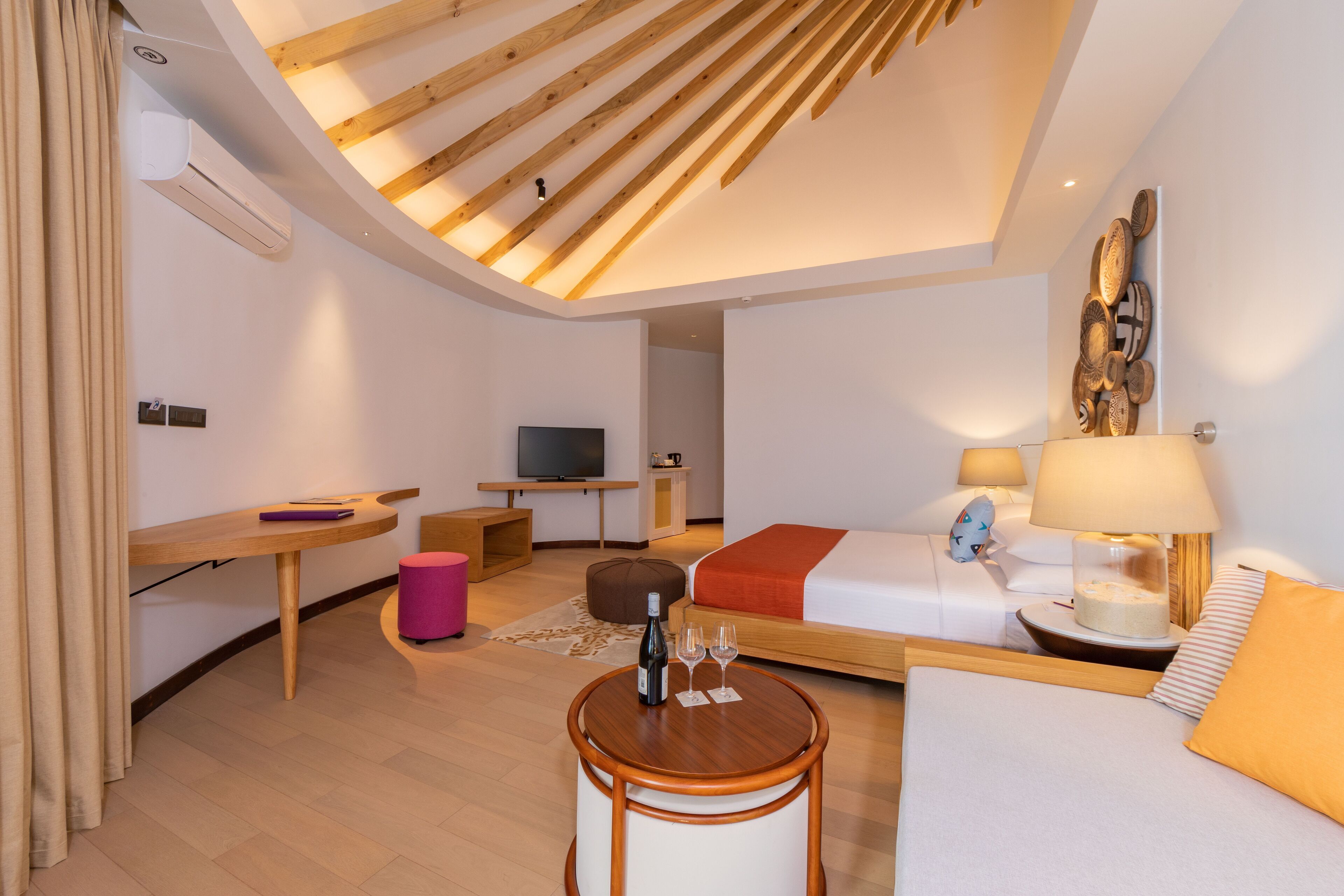 A modern hotel room with a loft bed, a desk, a television, and a dining area.