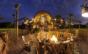 A rustic outdoor seating area with wooden chairs and a fire pit, surrounded by a wooden fence and palm trees. - Disney's Animal Kingdom Villas - Kidani Village (Kissimmee)
