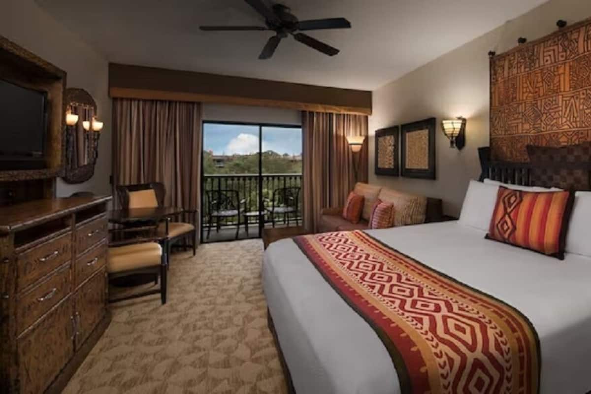 A hotel room with a large bed, a TV, a desk, and a balcony with a view.