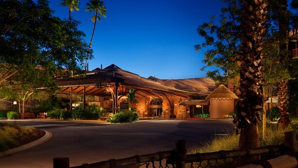 Un hotel con entrada cubierta, palmeras y un camino de acceso bien iluminado.