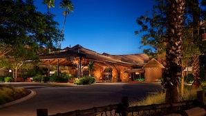 Un hotel con entrada cubierta, palmeras y un camino de acceso bien iluminado.
