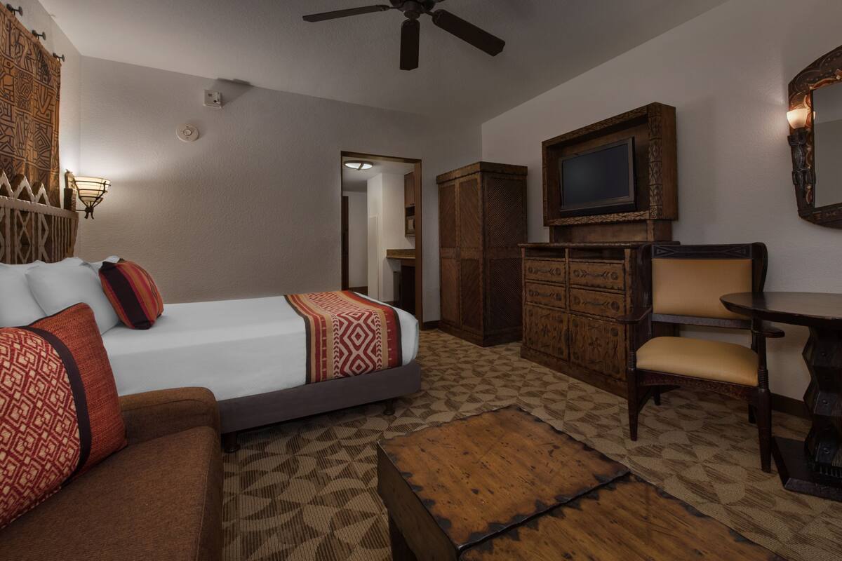 Ein Hotelzimmer mit Bett, Schlafsofa, Tisch, Stuhl, Kleiderschrank und Fernseher.