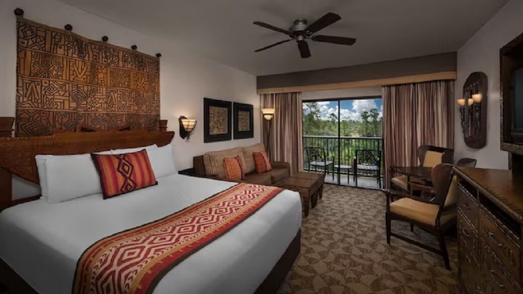 Una habitación de hotel con una cama grande, ventilador de techo, balcón con vistas y televisor.