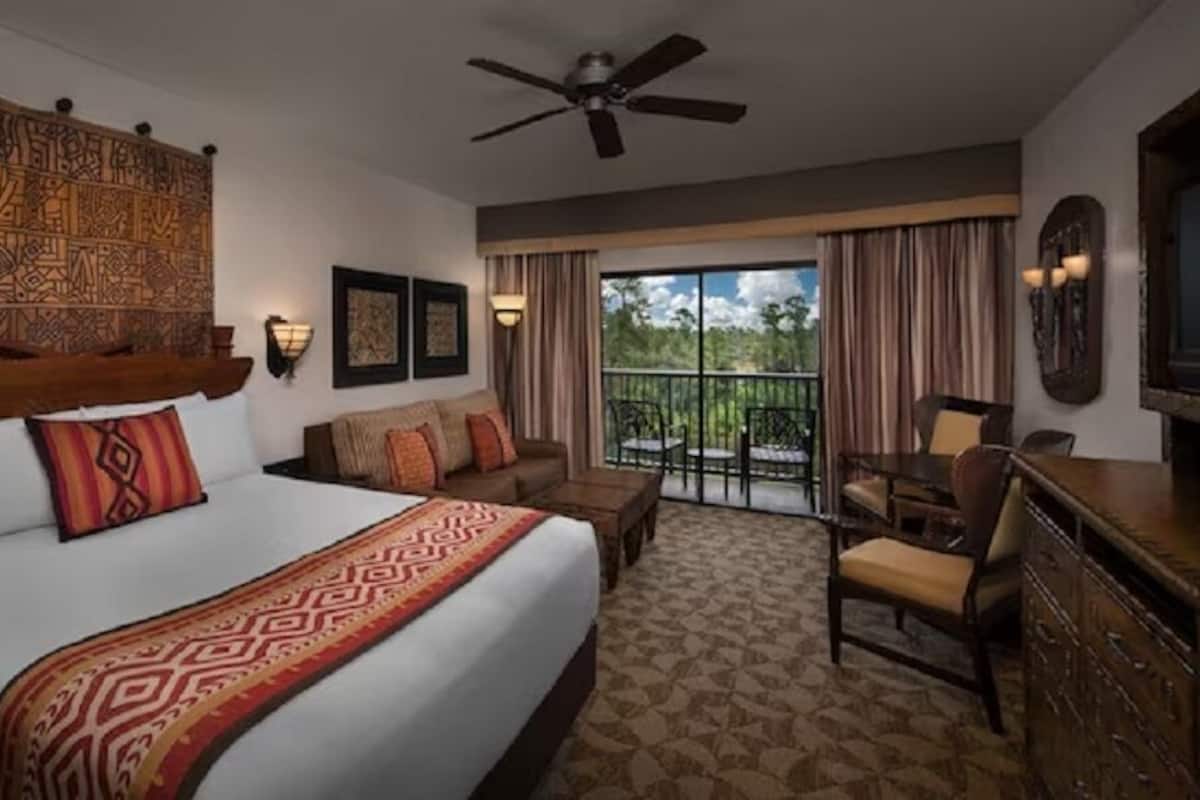 A hotel room with a large bed, a ceiling fan, a balcony with a view, and a television.