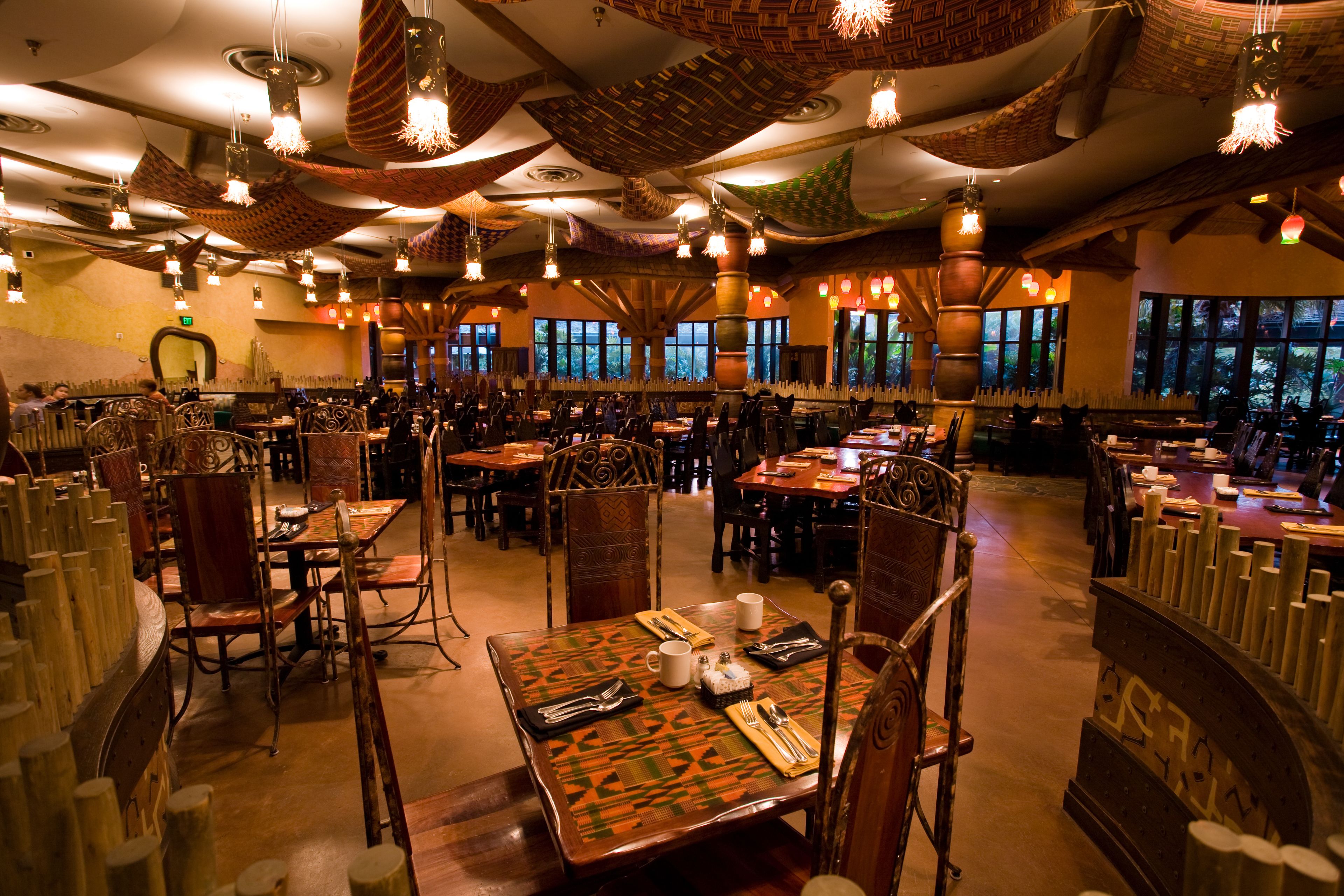 A restaurant with multiple dining tables and chairs, large windows, and hanging light fixtures.