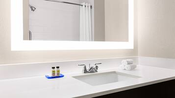Un baño con lavamanos blanco, espejo y zona de ducha.
