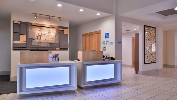 A hotel reception area with two reception desks, a modern wall-mounted display, and a tiled floor. - Holiday Inn Express & Suites San Antonio NW - Medical Area by IHG (San Antonio)
