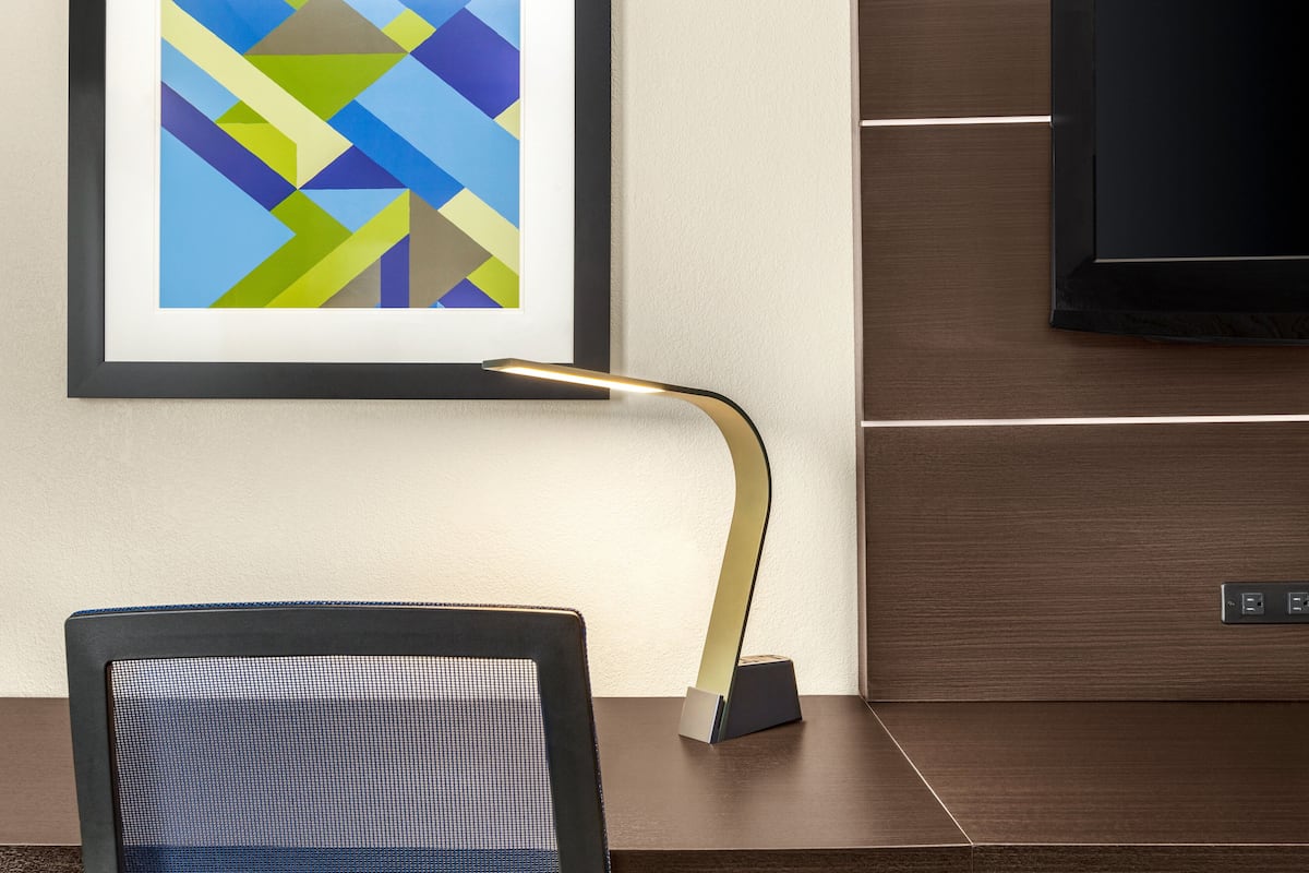 A modern office chair, a desk with a lamp, and a framed abstract painting on the wall.