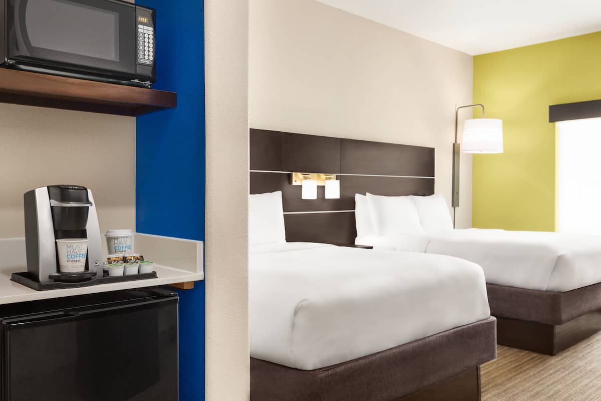 Habitación de hotel con kitchenette, dos camas, microondas, cafetera y refrigerador pequeño.