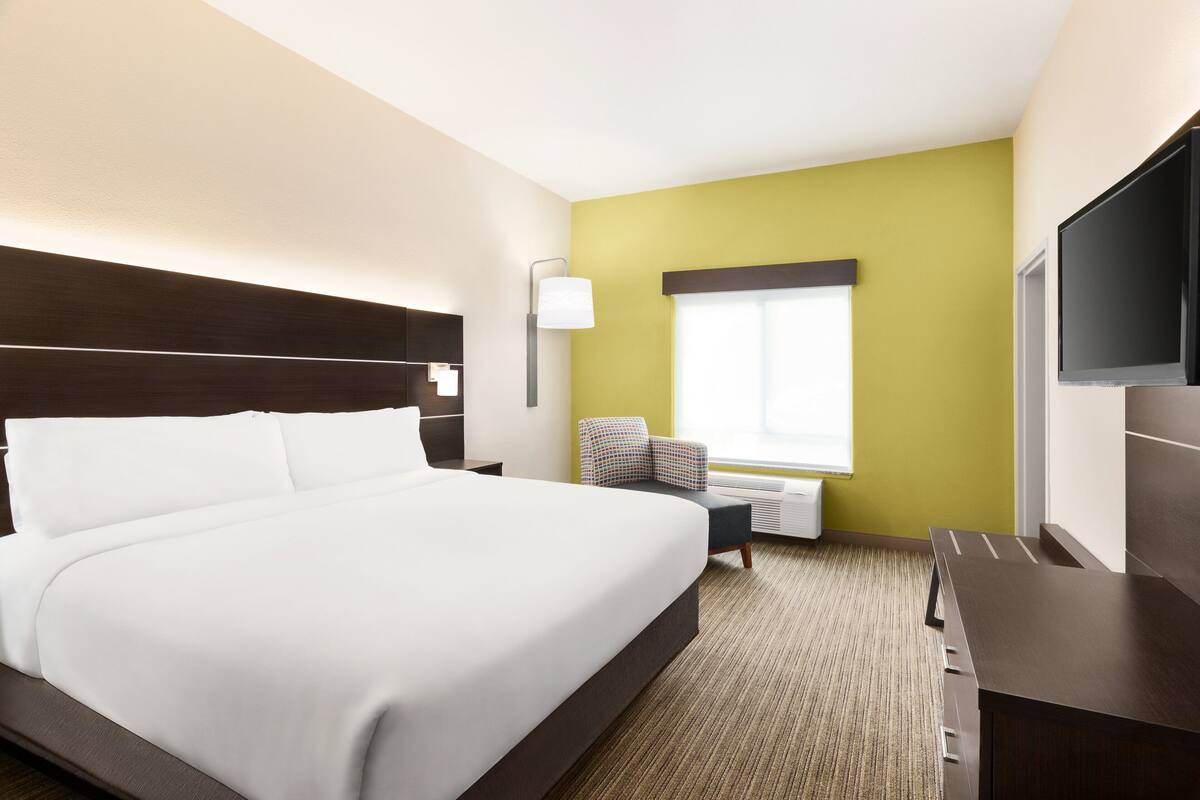 Habitación de hotel con una cama grande, un escritorio, una silla, un televisor y una ventana con persianas.