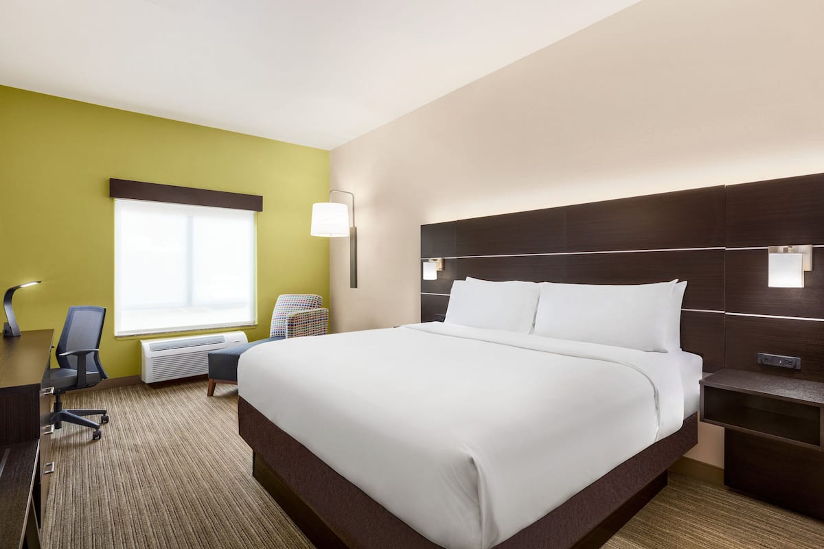 A hotel room with a large bed, a desk, a chair, a desk lamp, and a window.