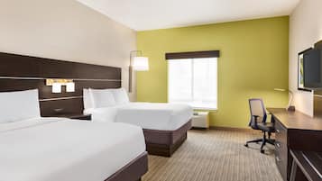 Habitación de hotel con dos camas, un escritorio, una silla, un televisor y una ventana con cortinas.