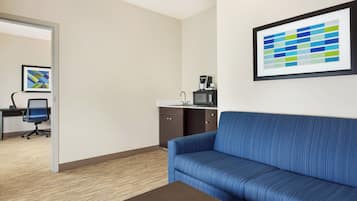 A hotel room with a blue sofa, a small table, a microwave, and a framed abstract art piece on the wall.
