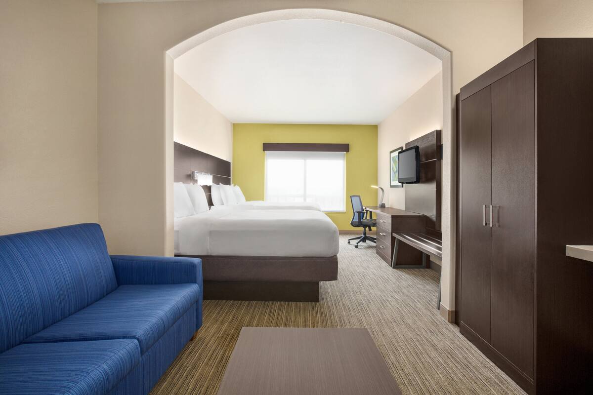 Una habitación de hotel con cama, sofá azul, escritorio, televisor y armario.