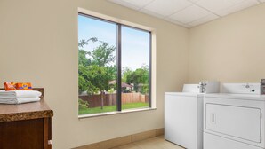 A laundry room with a large window, a washing machine, and a countertop with folded towels and laundry detergent. - Holiday Inn Express & Suites San Antonio NW - Medical Area by IHG (San Antonio)
