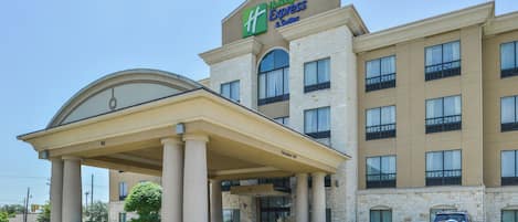 A Holiday Inn Express Suites building with a covered entrance, stone facade, and multiple windows.
