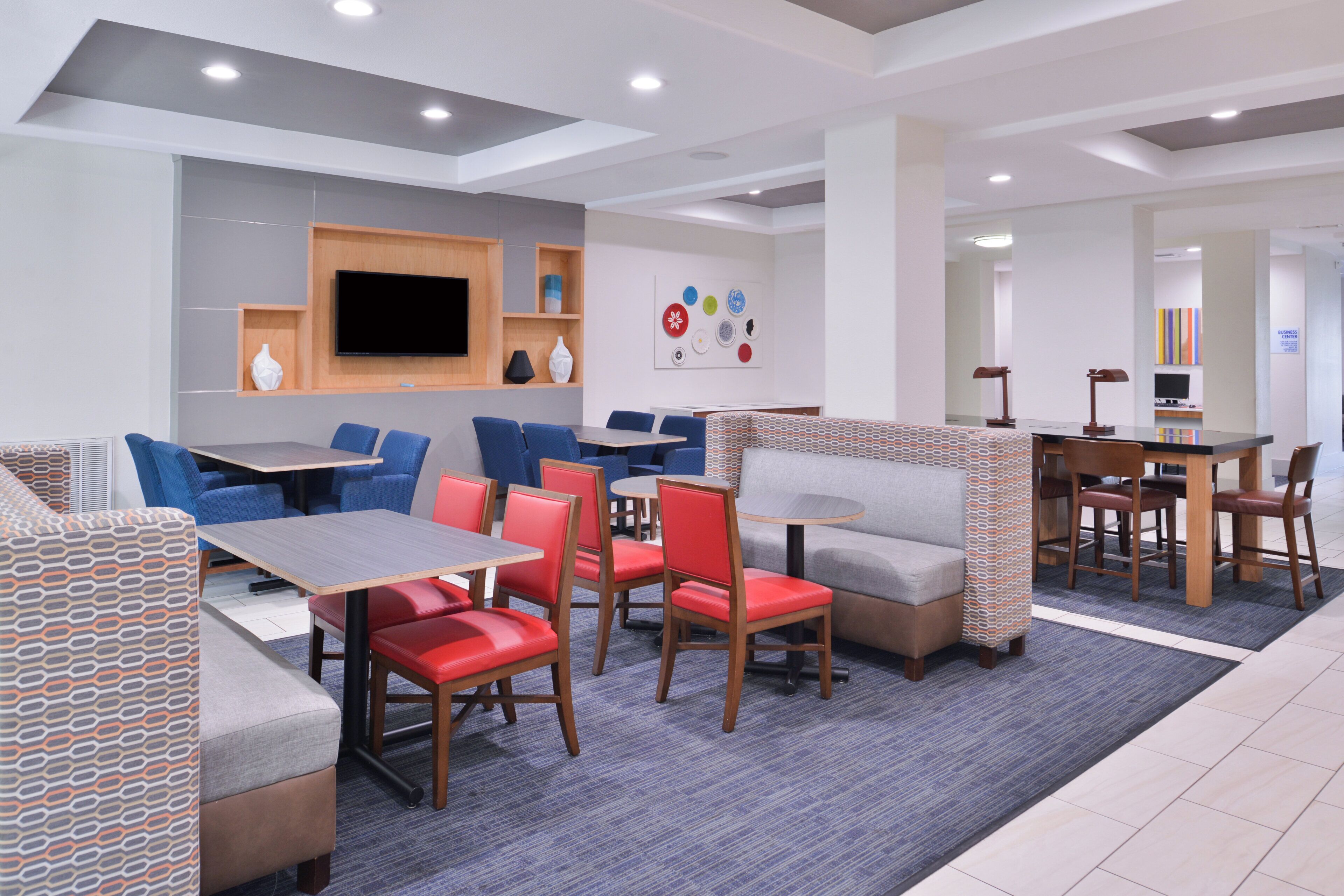 A modern dining area with multiple seating options including tables and chairs, a flat-screen TV mounted on the wall, and a decorative wall art piece.