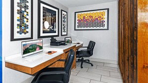 Un espace de bureau moderne avec un bureau en bois, deux chaises de bureau noires et des œuvres d’art encadrées accrochées au mur.