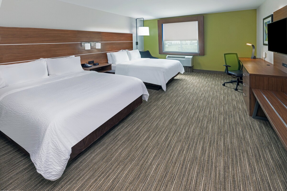 A hotel room with two beds, a desk, a chair, a TV, and a window with a view.