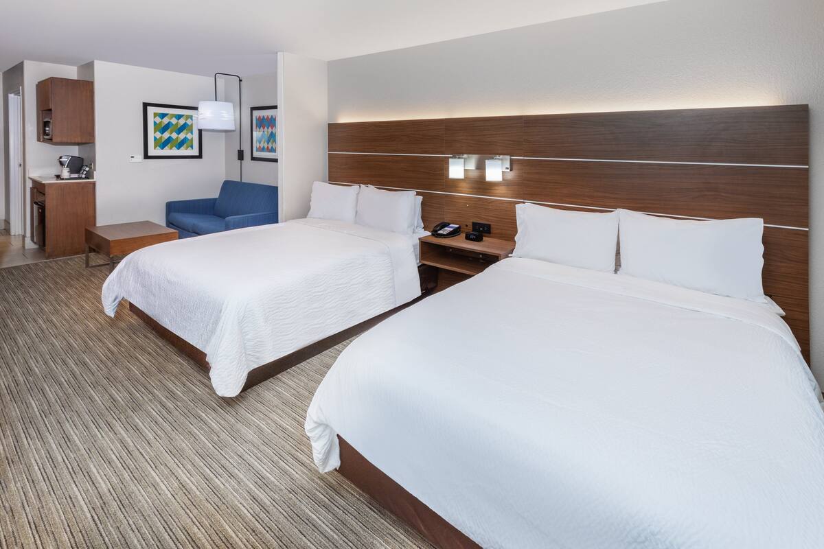 A hotel room with two beds, a desk, a chair, and a small kitchenette.
