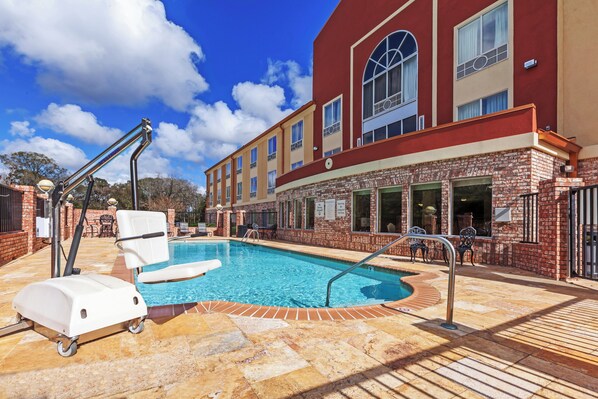 A hotel pool area with a wheelchair, a sun lounger, and a brick wall.