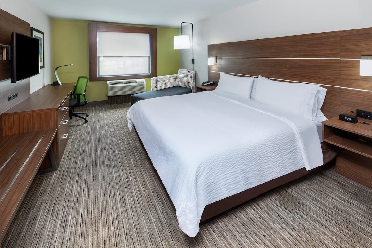 A hotel room with a large bed, a desk with a chair, a television, and a window with blinds.