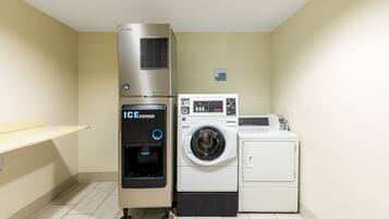 Une buanderie équipée d’un lave-linge et d’un sèche-linge superposés, d’un distributeur d’eau et d’un panneau indiquant l’emplacement.