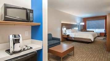 Habitación de hotel con cama, mesita de noche, lámpara y una pequeña cocina equipada con microondas y cafetera.