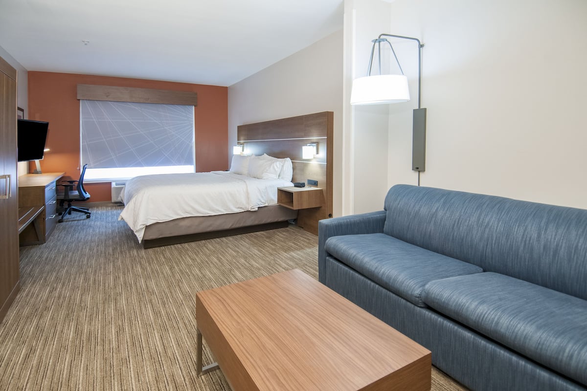 A hotel room with a bed, a sofa, a desk with a chair, a TV, and a lamp.