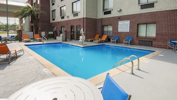 Una piscina con sillones de descanso y un detector de incendios en el edificio.