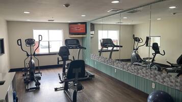 A gym with exercise equipment, a mirrored wall, and windows.