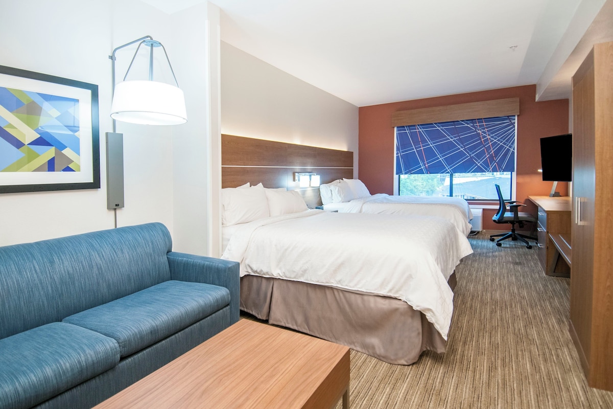 Una habitación de hotel con cama, escritorio, silla, sofá y un amplio ventanal.