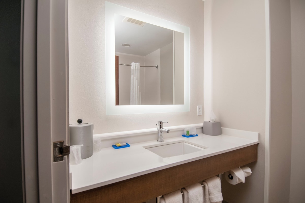 Un baño con un lavamanos blanco, un espejo y un perchero para toallas.