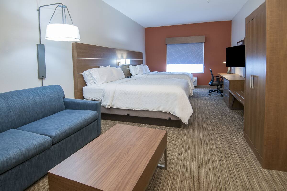 A hotel room with a bed, a sofa, a desk, a TV, and a lamp.