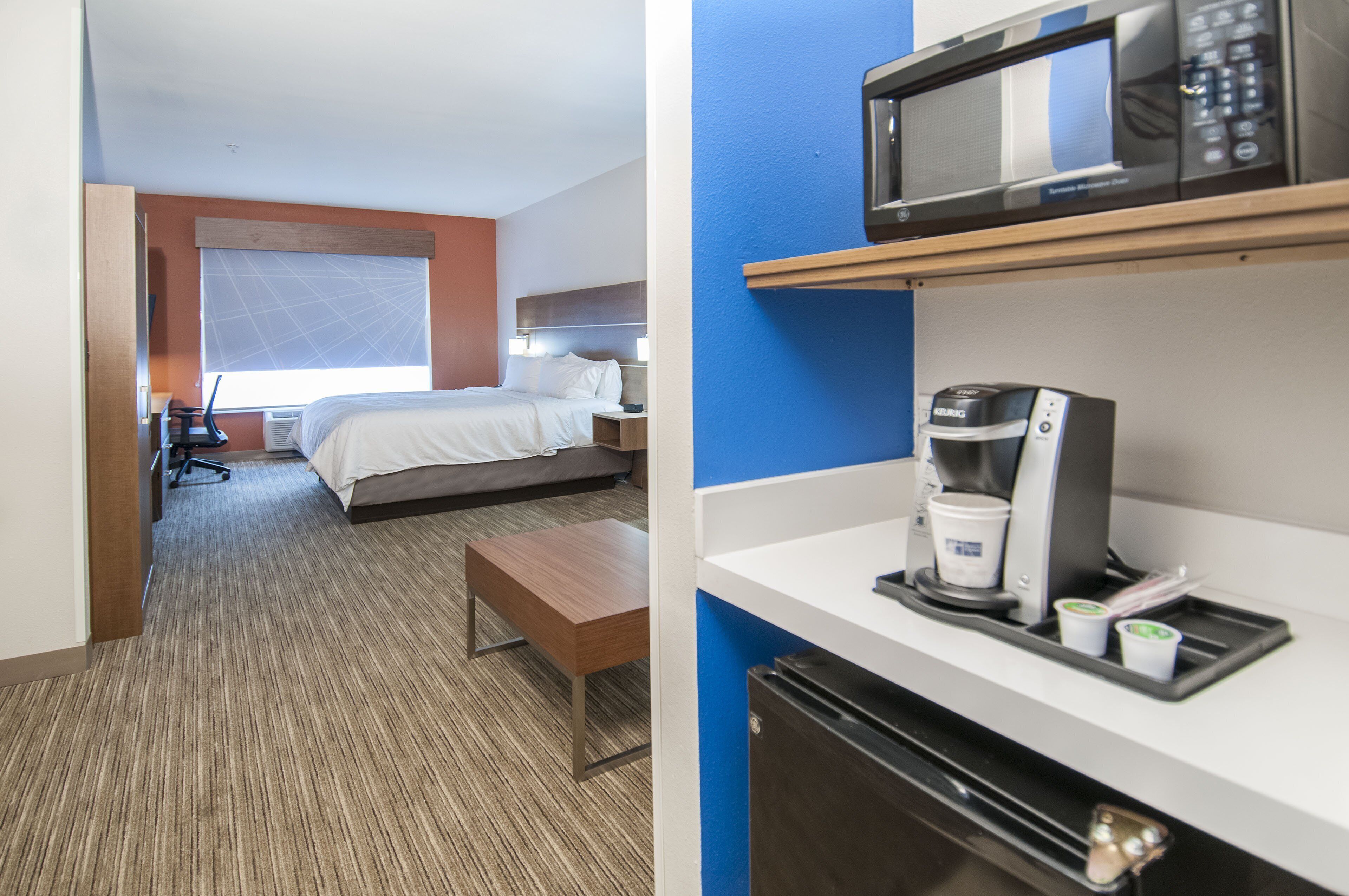 A hotel room with a bed, bedside table, and a desk with a chair. There is a window with a view of the outside.