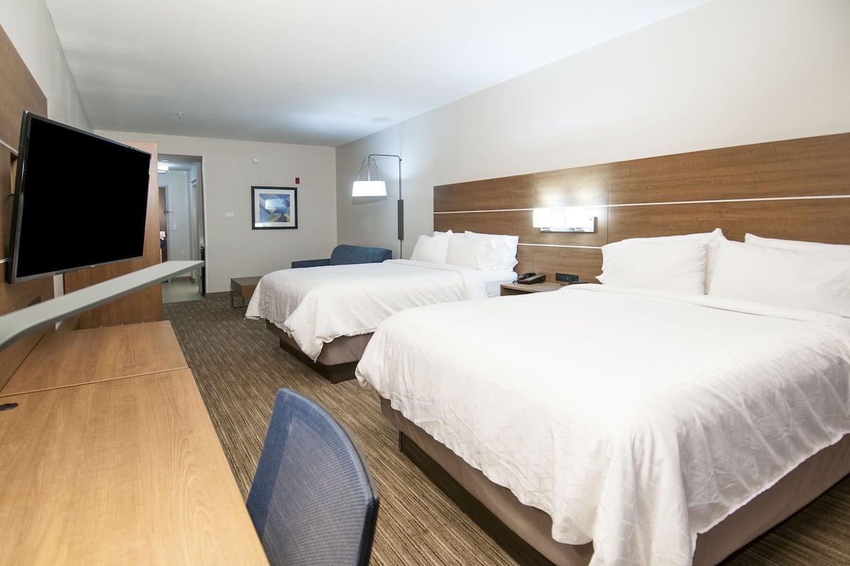 A hotel room with two beds, a desk, a chair, a TV, and a bedside table.