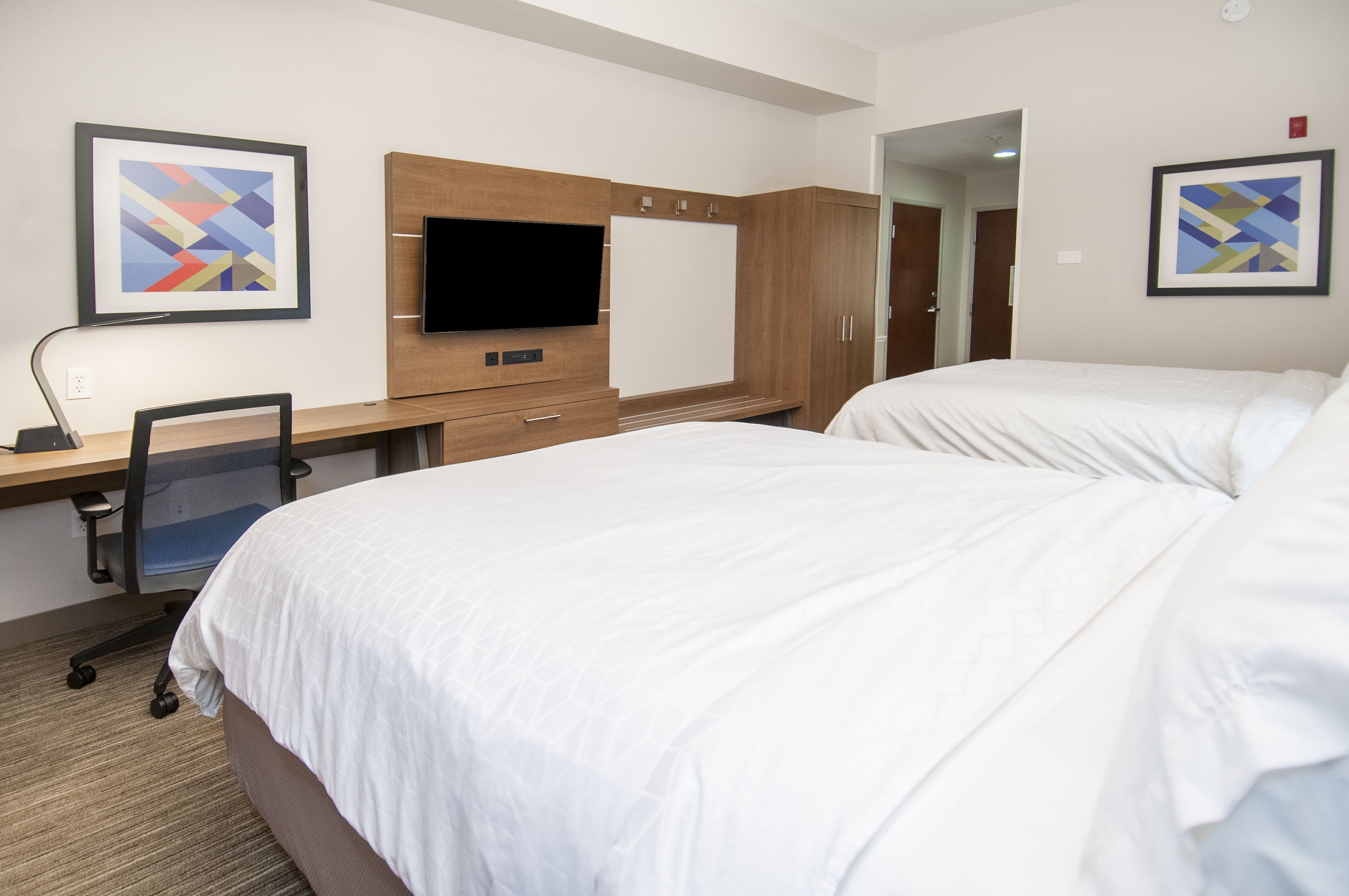 A hotel room with two beds, a desk with a chair, a flat-screen TV, and wooden cabinets.