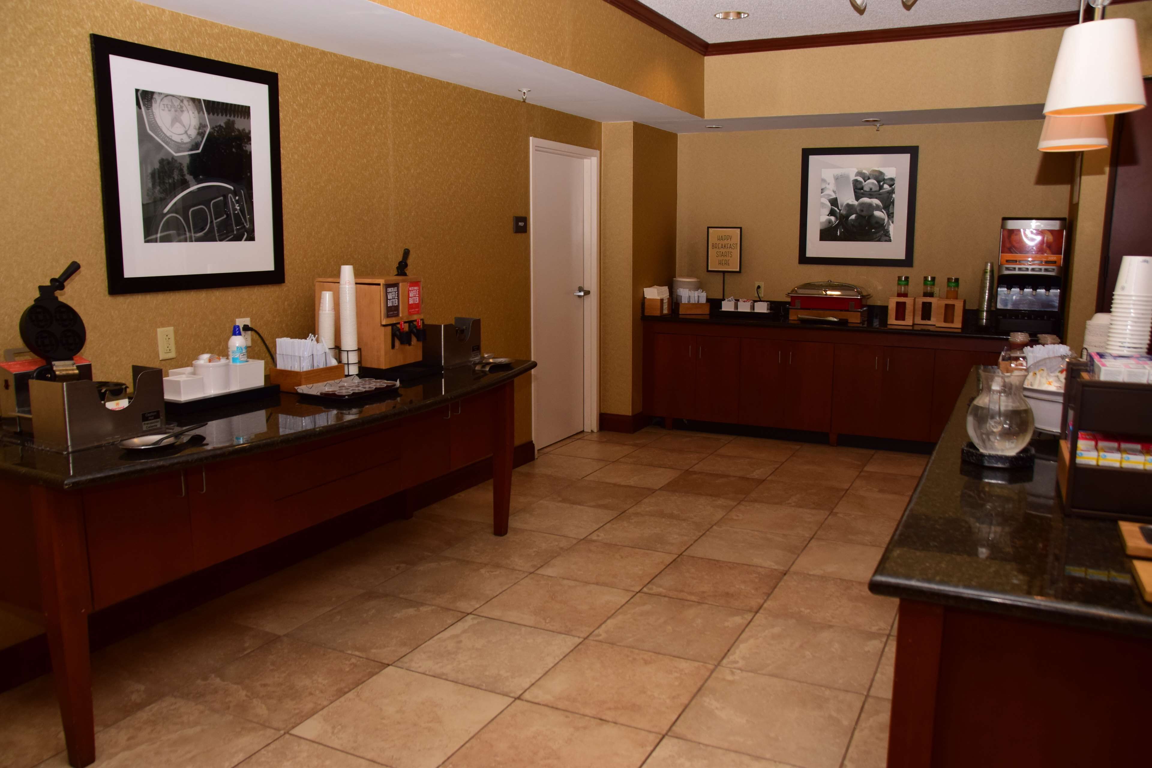 A hotel reception area with a reception desk, framed pictures on the wall, a coffee machine, and a counter with various items.