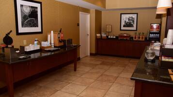 A hotel reception area with a reception desk, framed pictures on the wall, a coffee machine, and a counter with various items.