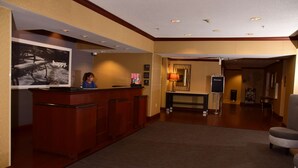 A reception area with a wooden desk, a receptionist, a welcome sign, and a framed picture on the wall. - Hampton Inn Indiana (Indiana)