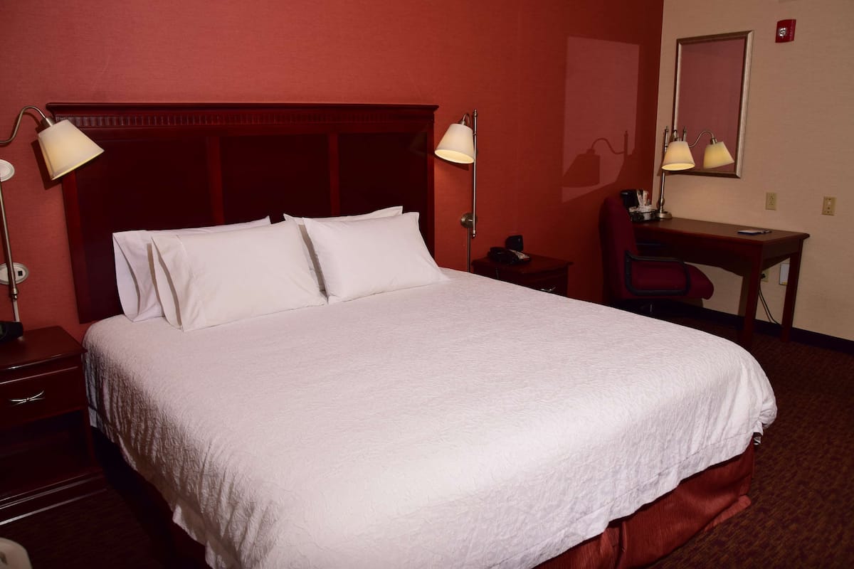 A hotel room with a large bed, two bedside lamps, a desk with a chair, and a mirror on the wall.